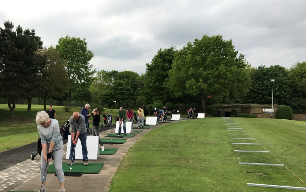 Golfen lernen - Gruppe von Anfängern auf der Driving Range